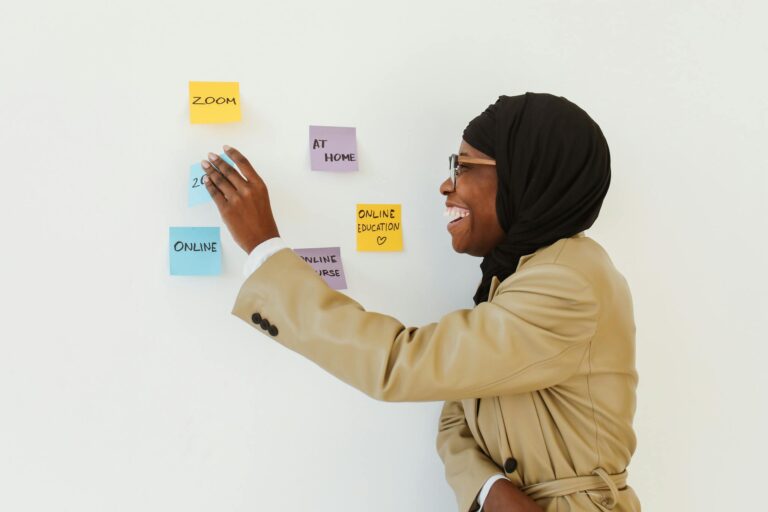A cheerful woman in a hijab arranging sticky notes for online education planning.